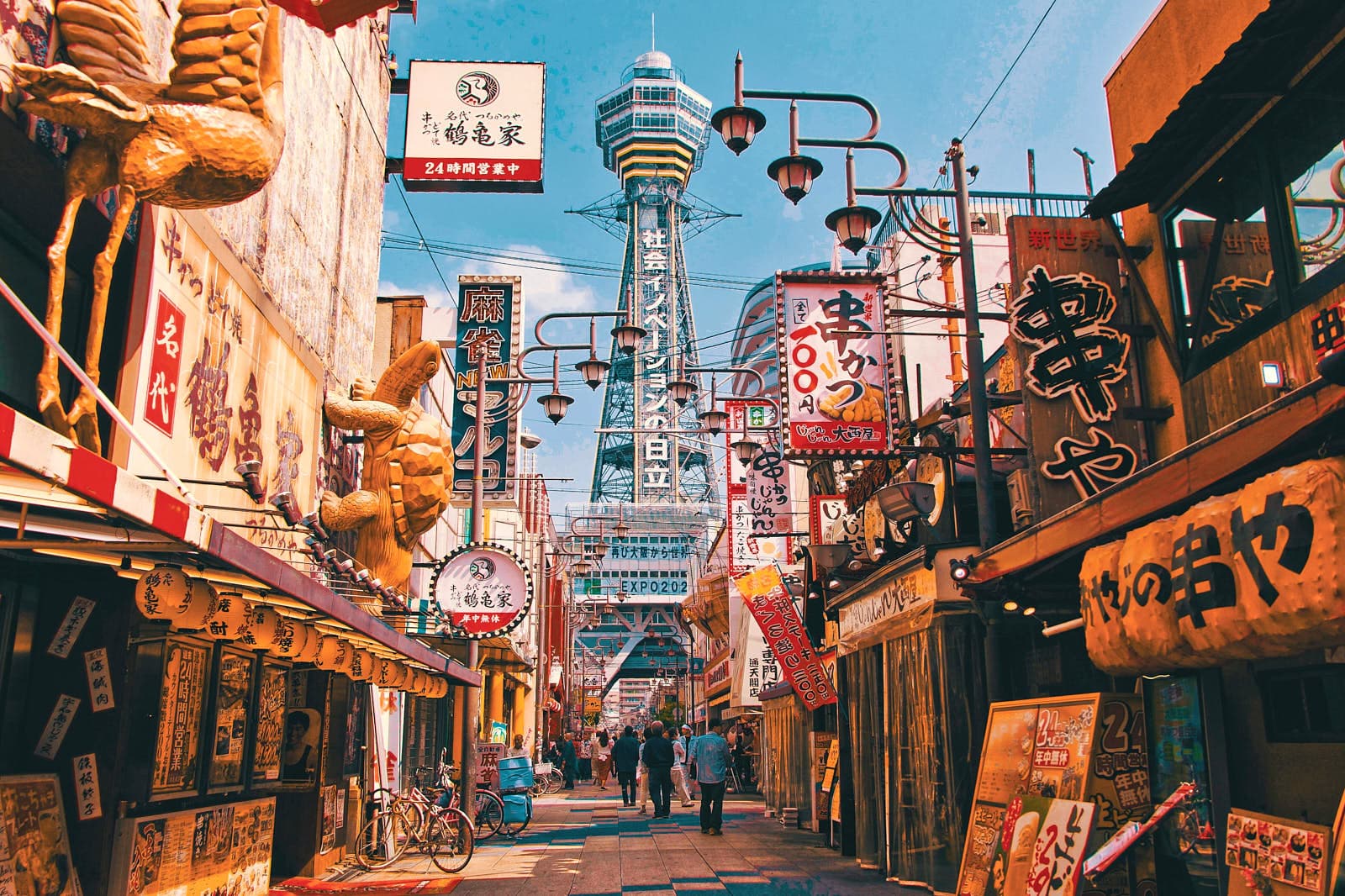 Shom paytidagi Osaka shahrining manzarasi: baland temiryo'l liniyalari, gavjum shahar ko'chalari va neon belgilari.