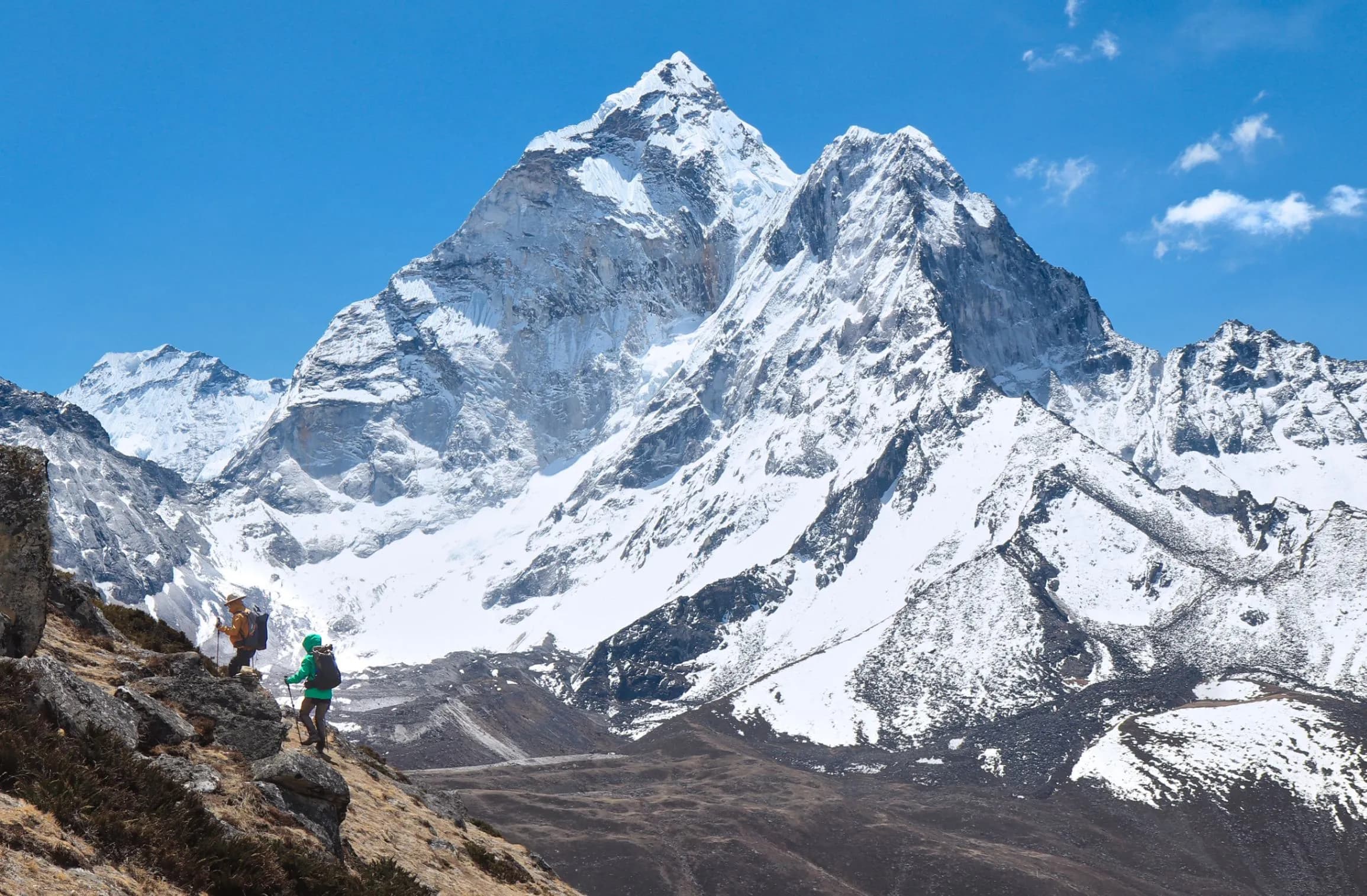 Orqa fonda qorli Himolay choʻqqilari koʻrinib turgan Everest bazaviy lageriga olib boruvchi soʻqmoqdagi trekkerlar.
